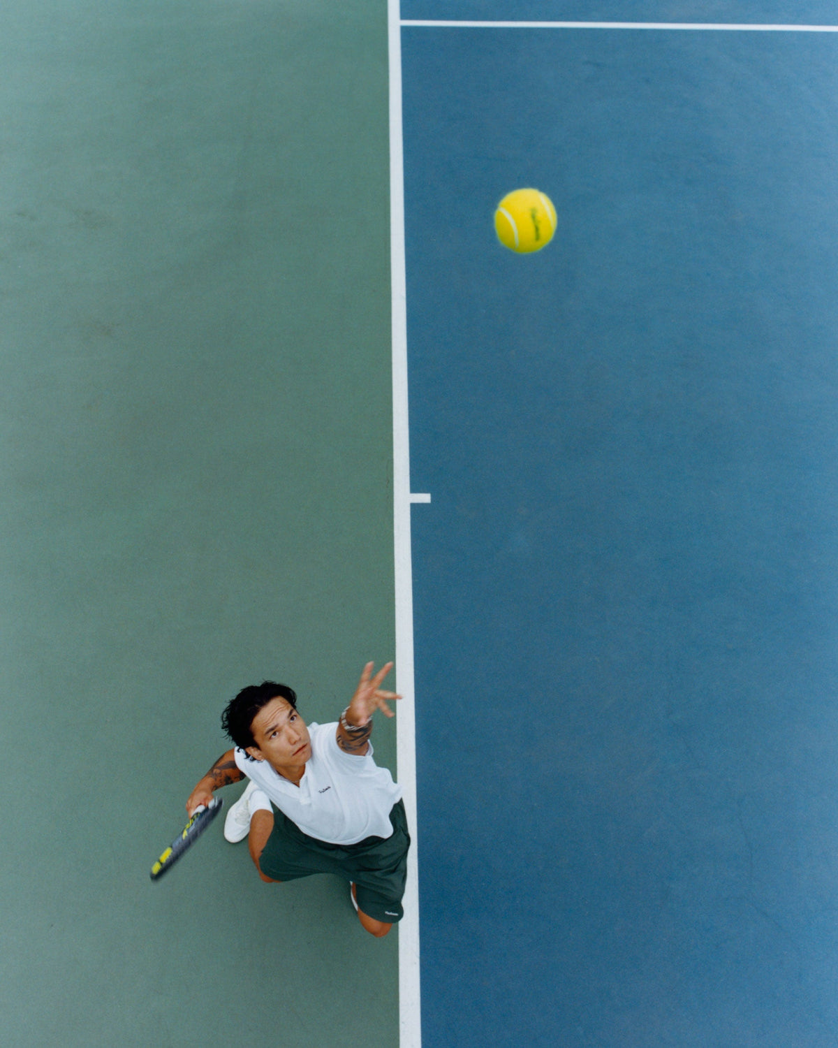 Overhead view of Alex Tan tossing a ball to serve on a blue tennis court